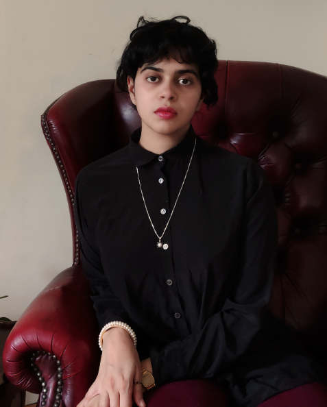 Aditi is sitting on a red "Matrix-like" chair wearing all back and somewhat scowling.